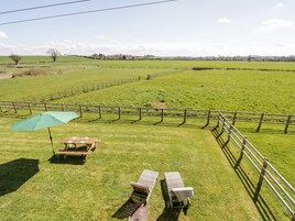 Un espacio al aire libre con césped, una mesa de madera y dos sillones, un paraguas verde y una valla de madera.