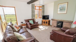 A living room with leather sofas, a television, a fireplace, and a large window with a view of the countryside. - Manor Farm Cottage (Worcester)