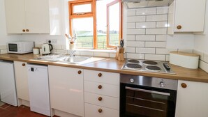 A modern kitchen with white cabinets, a built-in oven, a microwave, and a window with a view of the outdoors. - Manor Farm Cottage (Worcester)