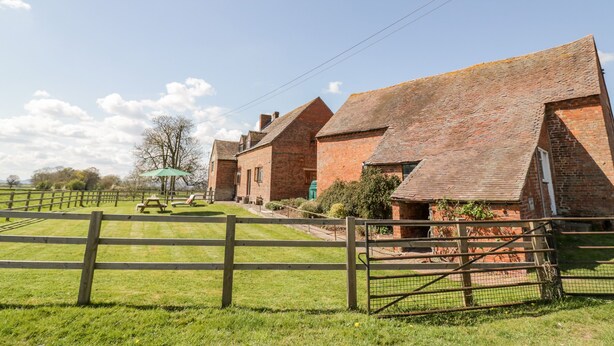 A brick farmstead with multiple buildings, a wooden fence, and a picnic area. - Manor Farm Cottage (Worcester)
