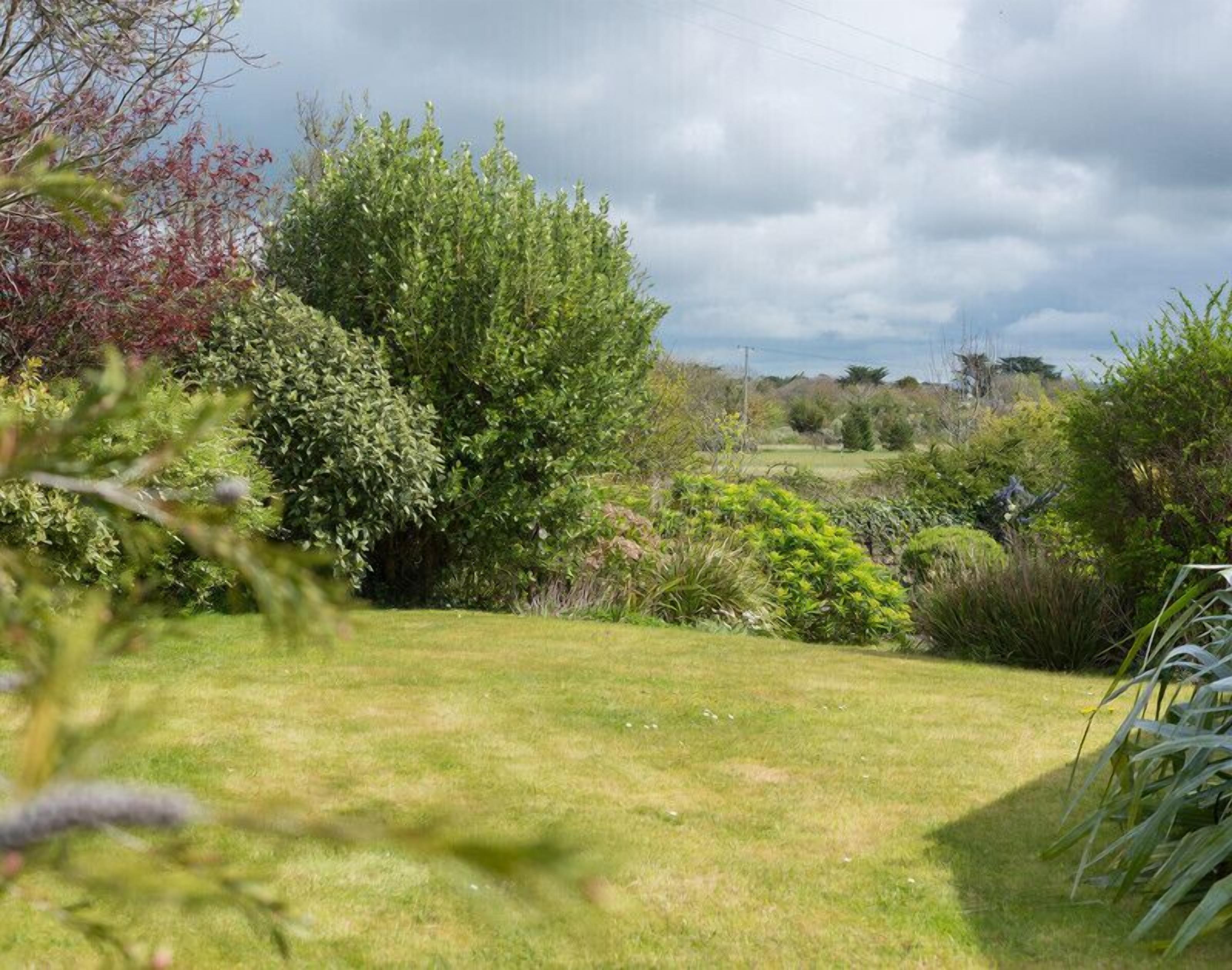 A lush garden with a variety of plants and trees, a well-maintained lawn, and a distant view of a field.