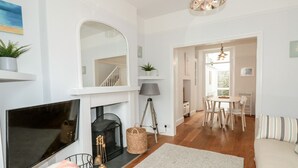 A modern living room with a fireplace, a flat-screen TV, a sofa, and a dining area with a table and chairs. - Bay Tree Cottage, Dartmouth (Dartmouth)
