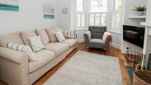 A living room with a beige sofa, a grey armchair, a TV, and a fireplace. - Bay Tree Cottage, Dartmouth (Dartmouth)