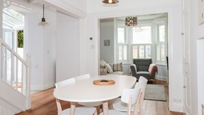 A dining area with a round white table, white chairs, and a hanging light fixture. - Bay Tree Cottage, Dartmouth (Dartmouth)