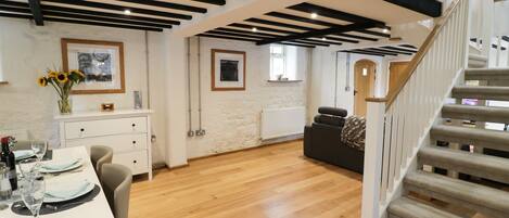 A spacious room with a wooden floor, a dining area with a white table set, a sofa, and a staircase with a carpeted handrail.