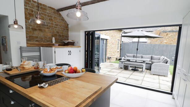 A modern kitchen with a large island, a dining area with outdoor seating, and a stone wall. - Hard Day's Night (Leicester)
