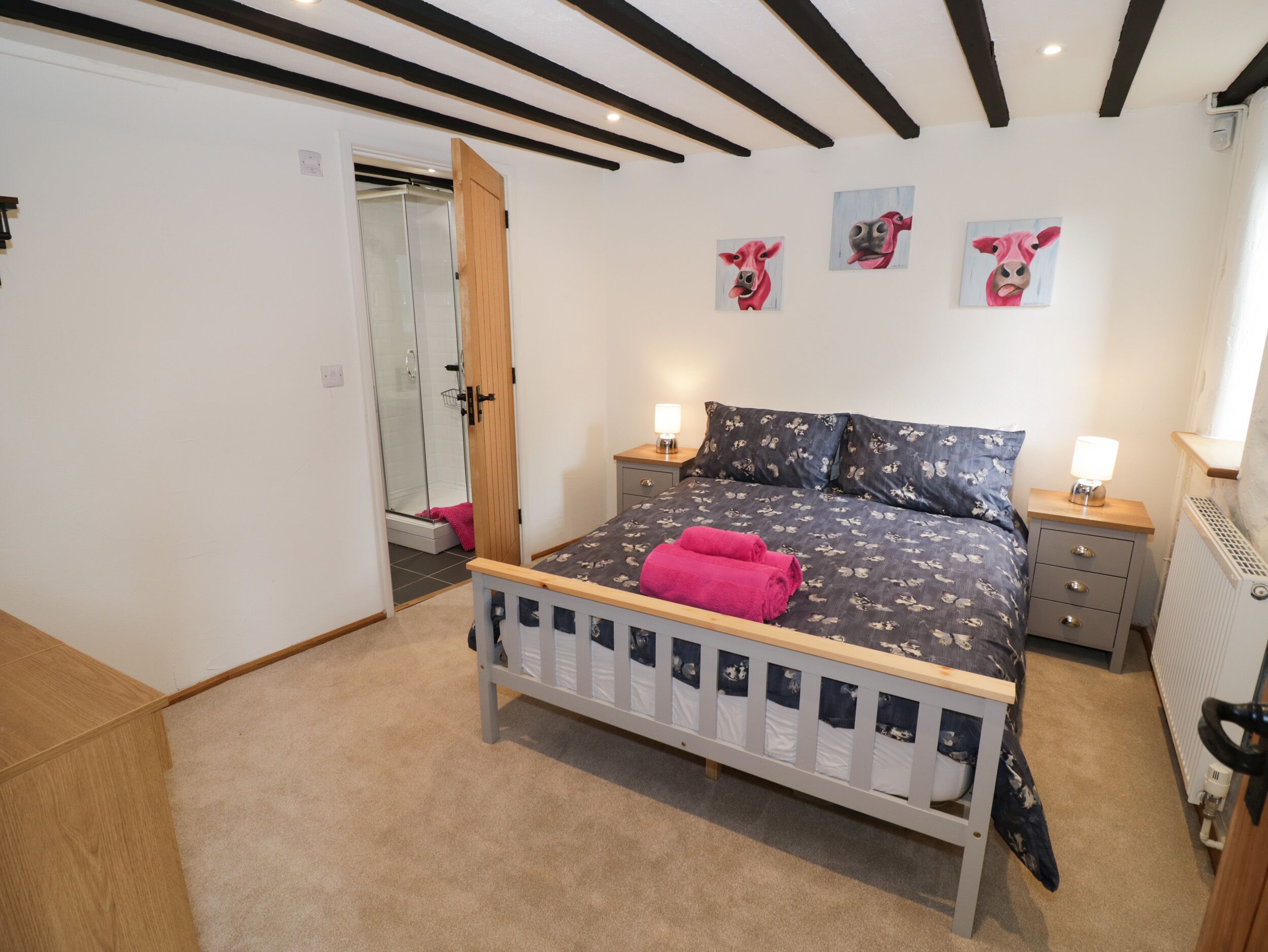 A bedroom with a bed, two bedside tables, a radiator, and a door leading to a shower area.