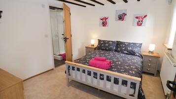 A bedroom with a bed, two bedside tables, a radiator, and a door leading to a shower area.