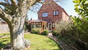 Une maison avec une véranda, un jardin et un grand arbre.