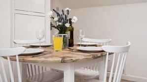 A dining area with a round wooden table, white chairs, and a vase with flowers. - Pinewood 14 (Wadebridge)