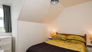 A bedroom with a bed, bedside lamps, a desk, and a window with curtains. - Pinewood 14 (Wadebridge)