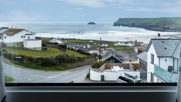 A coastal town with houses, a road, and a view of the sea and cliffs. - Pinewood 14 (Wadebridge)