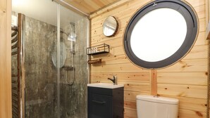 Casa de banho com chuveiro em cabine de vidro, espelho redondo e sanita.