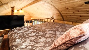 Um interior acolhedor de madeira com teto arredondado, uma cama com roupa de cama florida e uma televisão sobre um suporte.