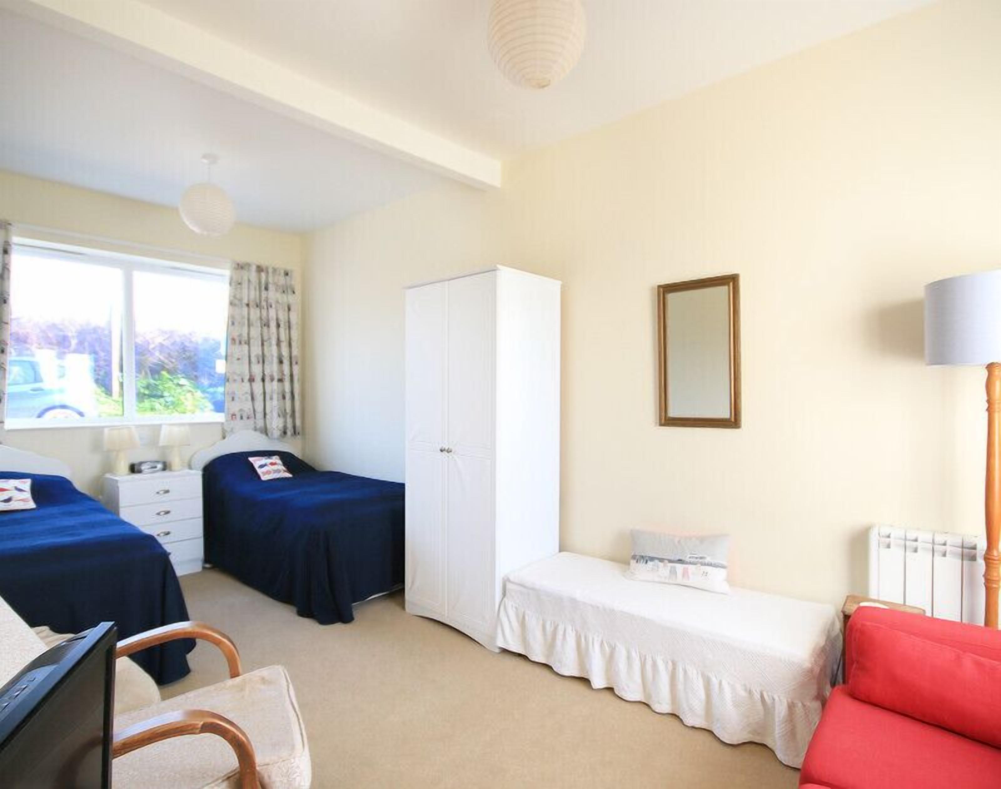 Une chambre avec deux lits, une armoire, un miroir, une lampe et un radiateur.