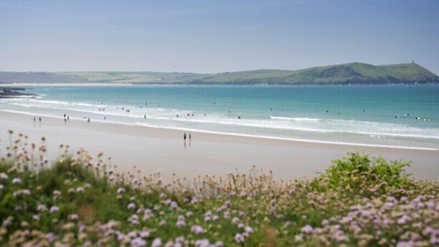 A beach with people walking along the shore and a hill in the background.