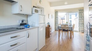 A compact kitchen with white cabinets, a microwave, and a stove. There is a dining area with a table and chairs, and a window with curtains.