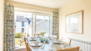 A dining area with a table set for four, a window with curtains, and a framed picture on the wall.