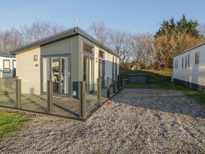 A modern mobile home with a glass door entrance, a deck, and a gravel driveway.