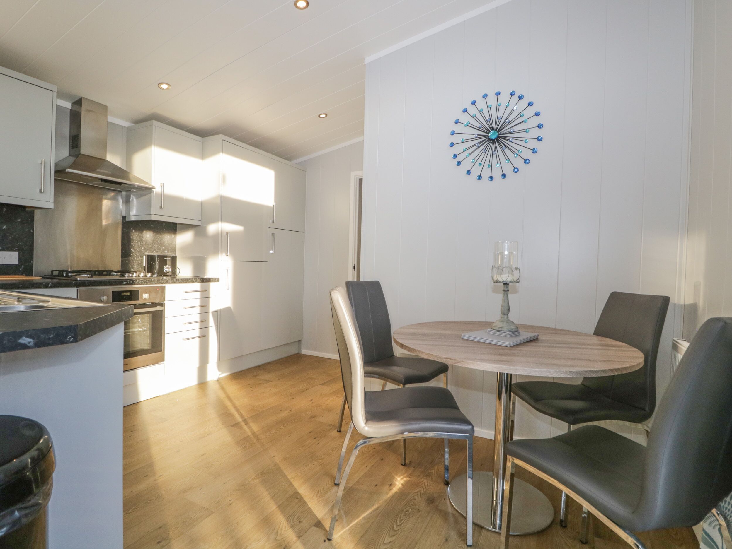 A modern kitchen with stainless steel appliances, a dining area with a round table and four chairs, and a decorative wall piece.