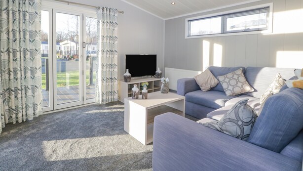 A modern living room with a grey sofa, a flat-screen TV, and a coffee table. There is a sliding glass door leading to a balcony. - Yealand 36 (Carnforth)