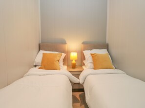 A twin room with two beds, each with white bedding and a single orange pillow. There is a nightstand between the beds with a lamp.