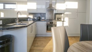 A modern kitchen with white cabinets, a stainless steel range hood, a built-in oven, and a black countertop. - Yealand 36 (Carnforth)