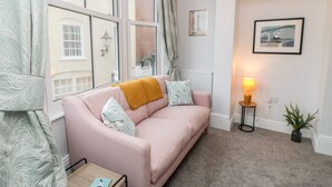 A cozy room with a pink sofa, a small table, a lamp, and a framed picture on the wall.