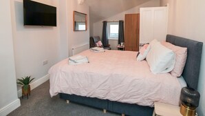 A bedroom with a bed, a TV, a mirror, a wardrobe, and a small table.
