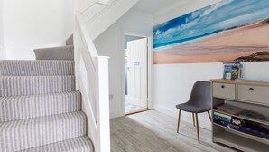 Un escalier recouvert d’une moquette à rayures, un bureau avec des livres et une fresque représentant une plage sur le mur.