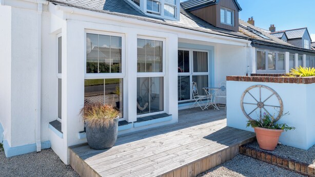 Une maison blanche avec de grandes fenêtres, une terrasse en bois et une brouette.