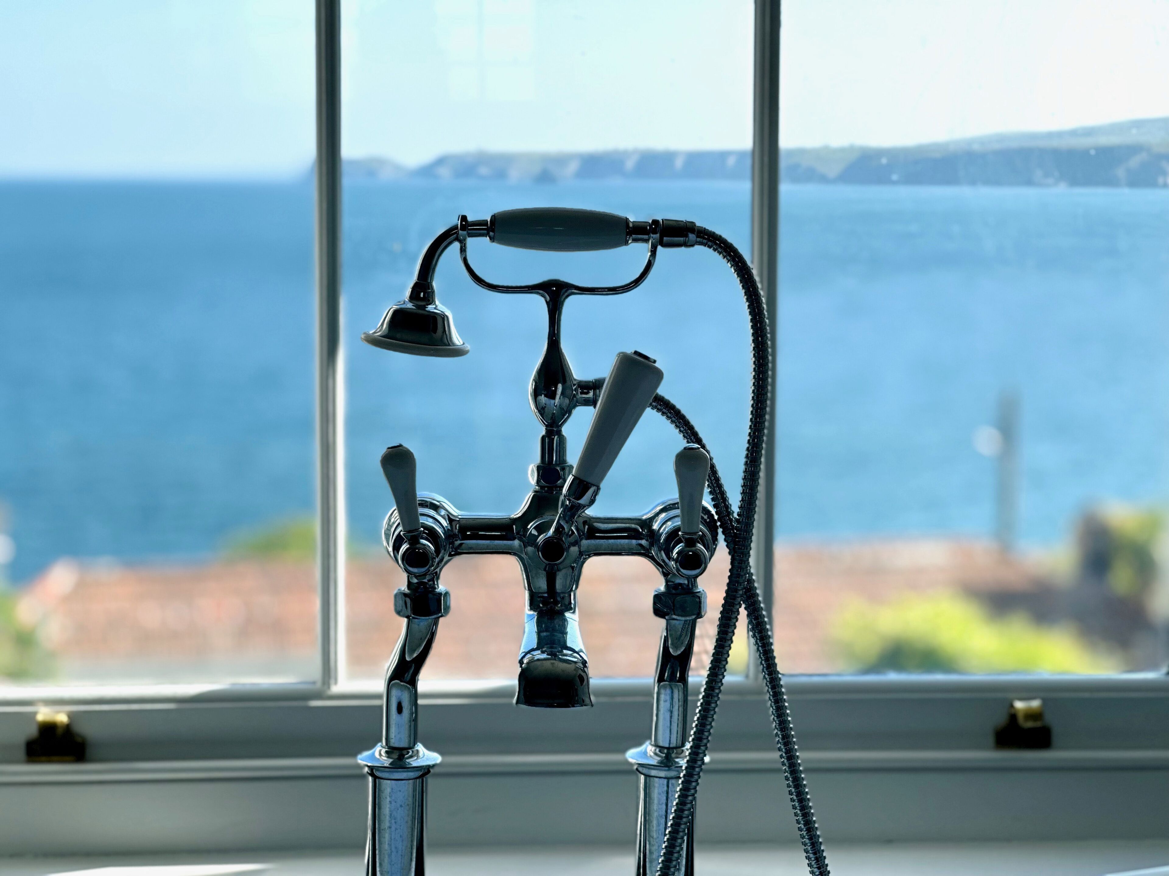 A bathroom with a shower head and a view of the sea through a window.