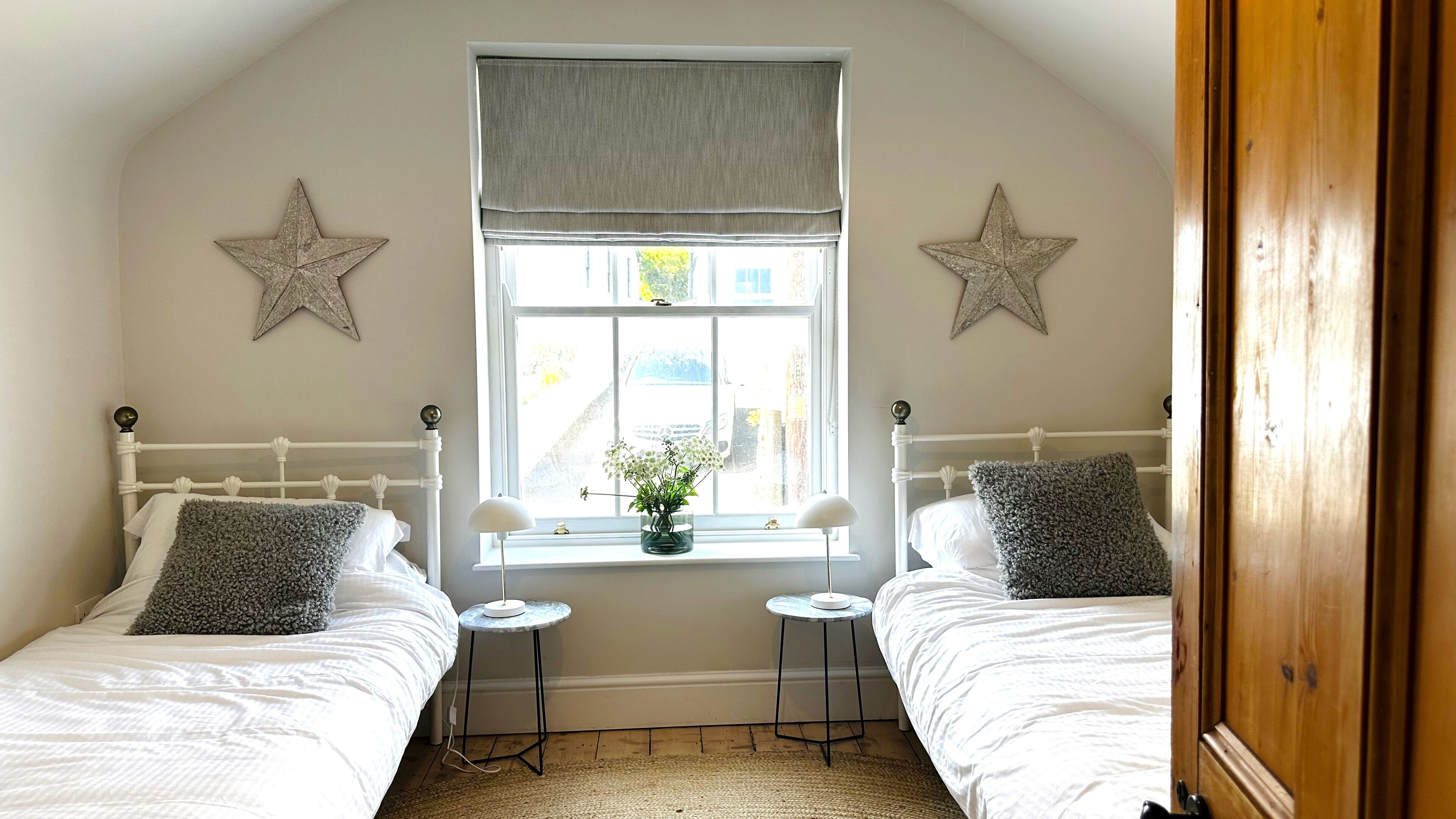 Quarto com duas camas de solteiro, janela com vista para a rua e estrelas decorativas nas paredes.