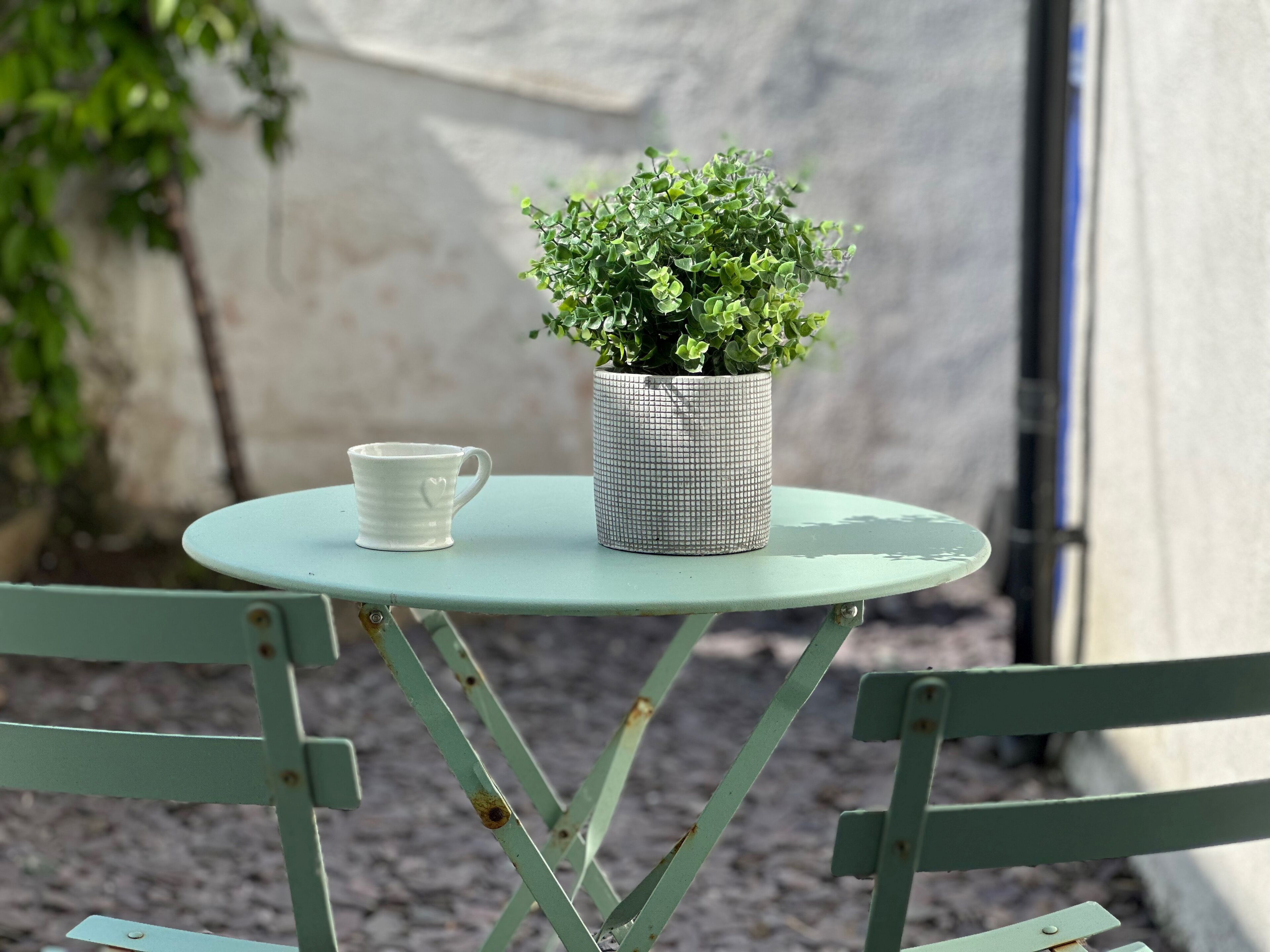 Una mesa redonda pequeña con una taza de cerámica blanca y una planta en maceta.