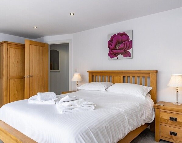 A bedroom with a wooden bed, white bedding, a wooden wardrobe, and a large purple flower painting on the wall.
