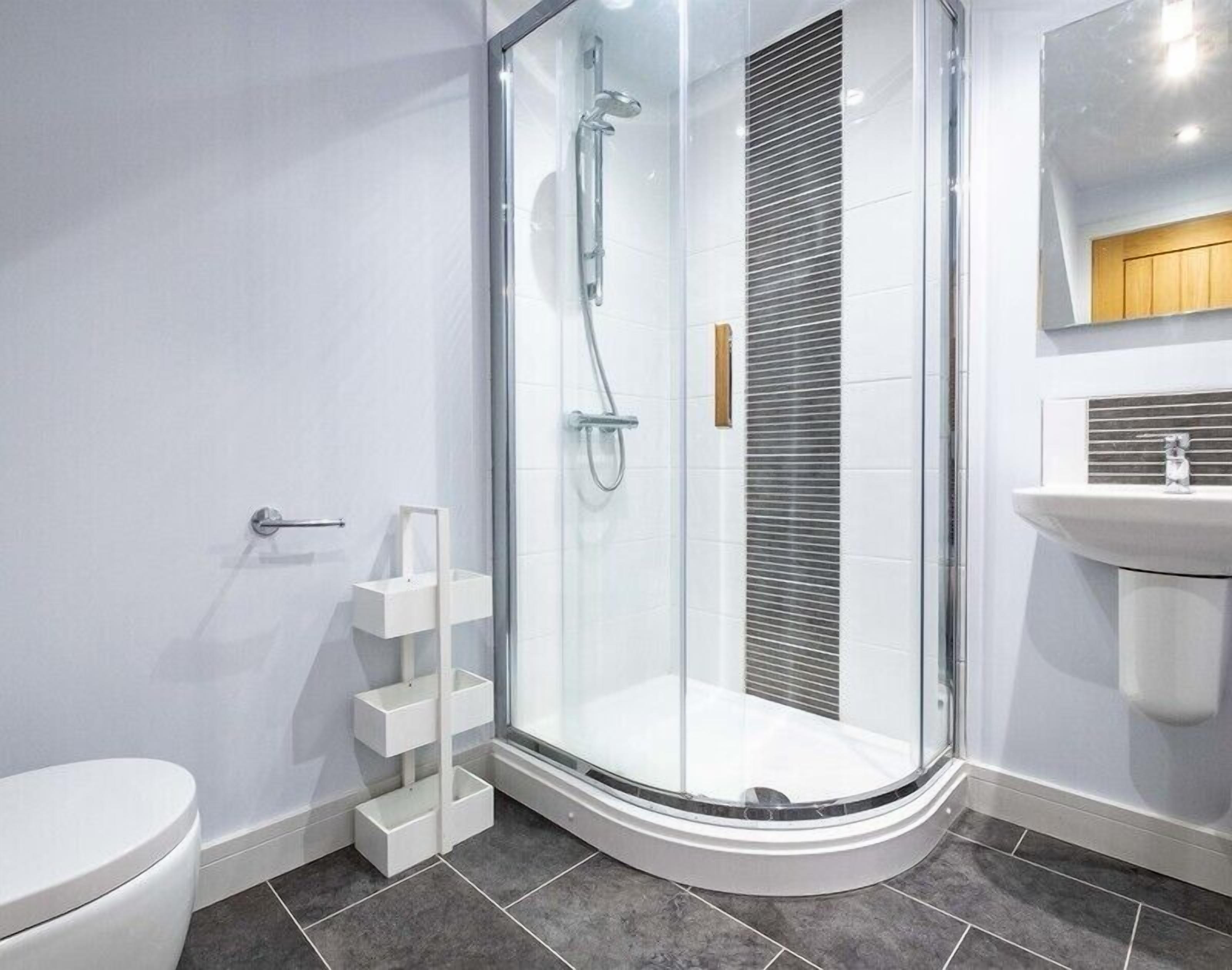 Une salle de bain moderne avec une douche à parois de verre, des toilettes blanches et un lavabo surmonté d’un meuble en bois.