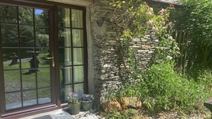 A stone building with a large glass door, potted plants, and a garden area. - Downrow Barn (Tintagel)