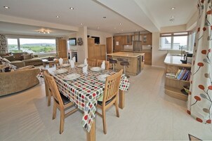 Un salón comedor amplio con una mesa dispuesta para cuatro comensales, una cocina con armarios de madera y vistas al campo.