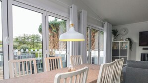 A dining area with a table, chairs, and a pendant light. - The Warren D7 (Pwllheli)