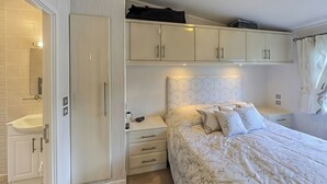 A bedroom with a bed, a nightstand, a dresser, and a built-in wardrobe. - The Warren D7 (Pwllheli)