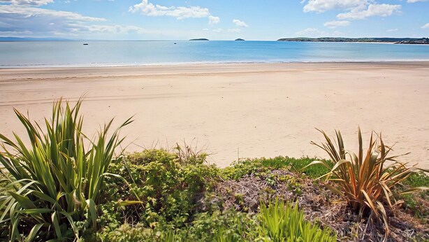A beach with clear skies, calm water, and distant islands. - The Warren D7 (Pwllheli)