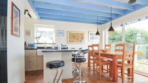 A modern kitchen with a bar stool, wooden dining table, and chairs. - Beachside (Wadebridge)