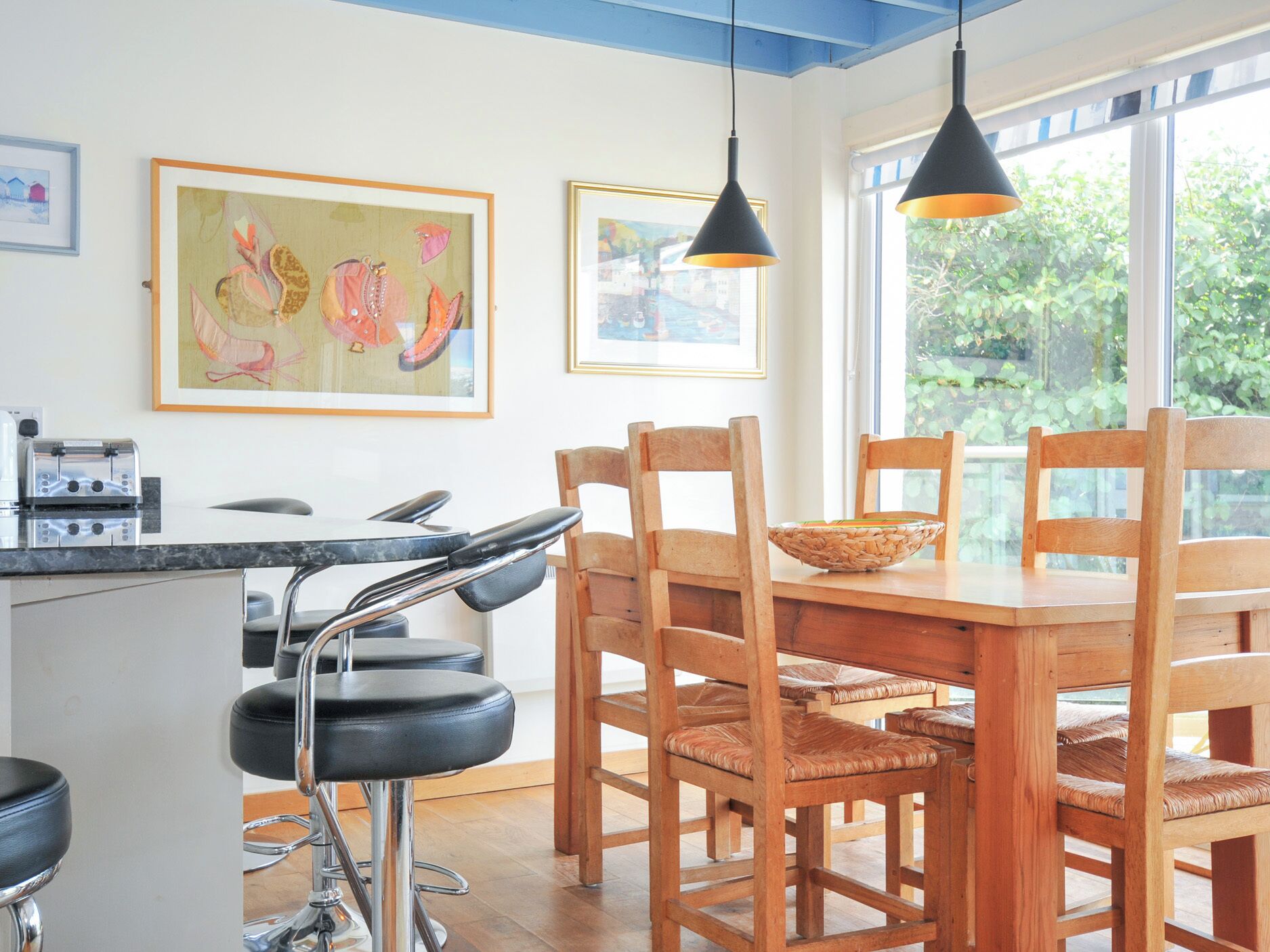 A kitchen with a marble countertop, a toaster, and a wooden dining table with chairs. There are two hanging pendant lights above the table.