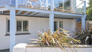 A two-story house with a balcony, clear glass railings, and a patio area with chairs and a table. - Beachside (Wadebridge)