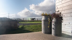 A rustic outdoor area with a wooden fence, metal barrels with flowers, and a grassy field. - Fell Briggs Cottage (Redcar)