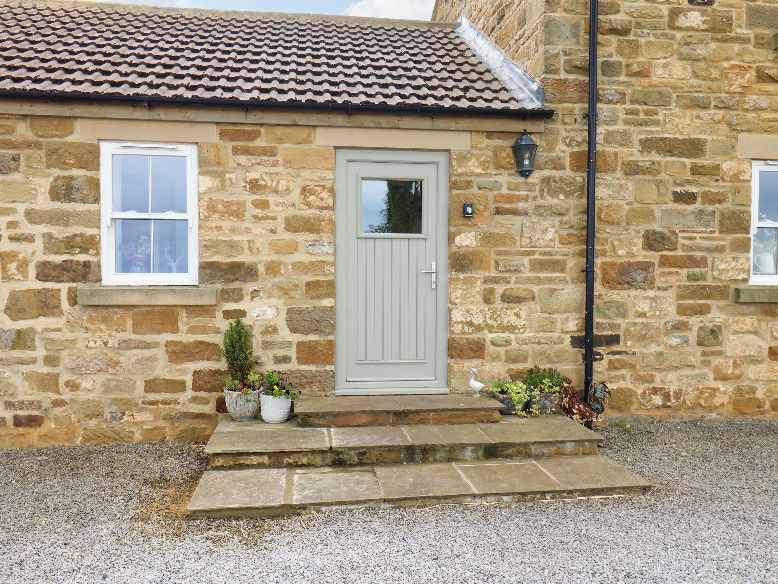 A stone building with a tiled roof, a door, and steps leading to the entrance.