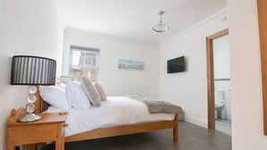 A bedroom with a bed, a bedside table, a lamp, a window, a painting, and a television. - Fell Briggs Cottage (Redcar)