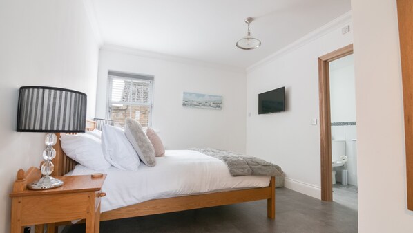A bedroom with a bed, a bedside table, a lamp, a window, a painting, and a television. - Fell Briggs Cottage (Redcar)