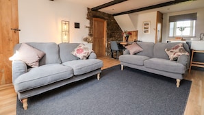A cozy living room with two grey sofas, a dark rug, wooden beams, a stone wall, and a wooden door. - Moss Side Retreat (Skipton)