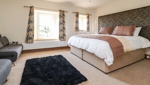 A bedroom with a bed, a sofa, a window with curtains, and a radiator. - Moss Side Retreat (Skipton)